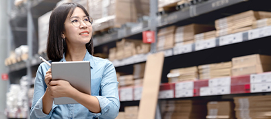 female worker taking inventory on tablet with high shelves of products in background