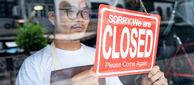 business owner holding store's door sign reading, "Sorry, we are closed. Please come again"