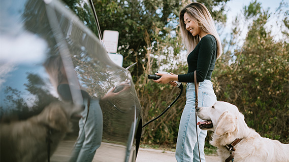 Woman charging her electric vehicle with her dog