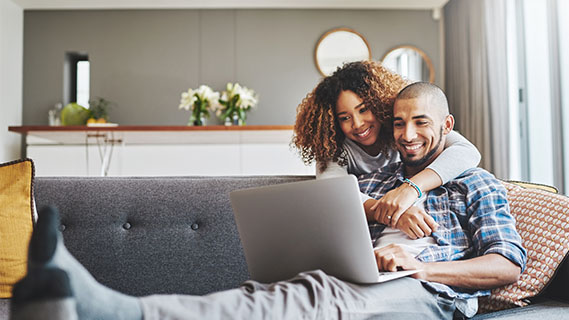 a young black couple on their couch on a laptop