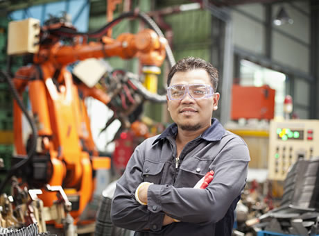 industrial worker with gloves and safety glasses crossing his arms in front of large-scale robotic assembly machinery